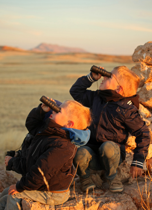 Zwei Kinder mit Fernglas auf Steinen