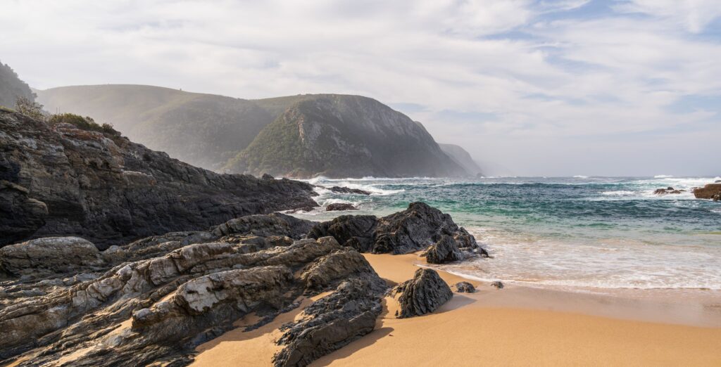 Bucht mit Sandstrand, Wellen und felsiger Küste