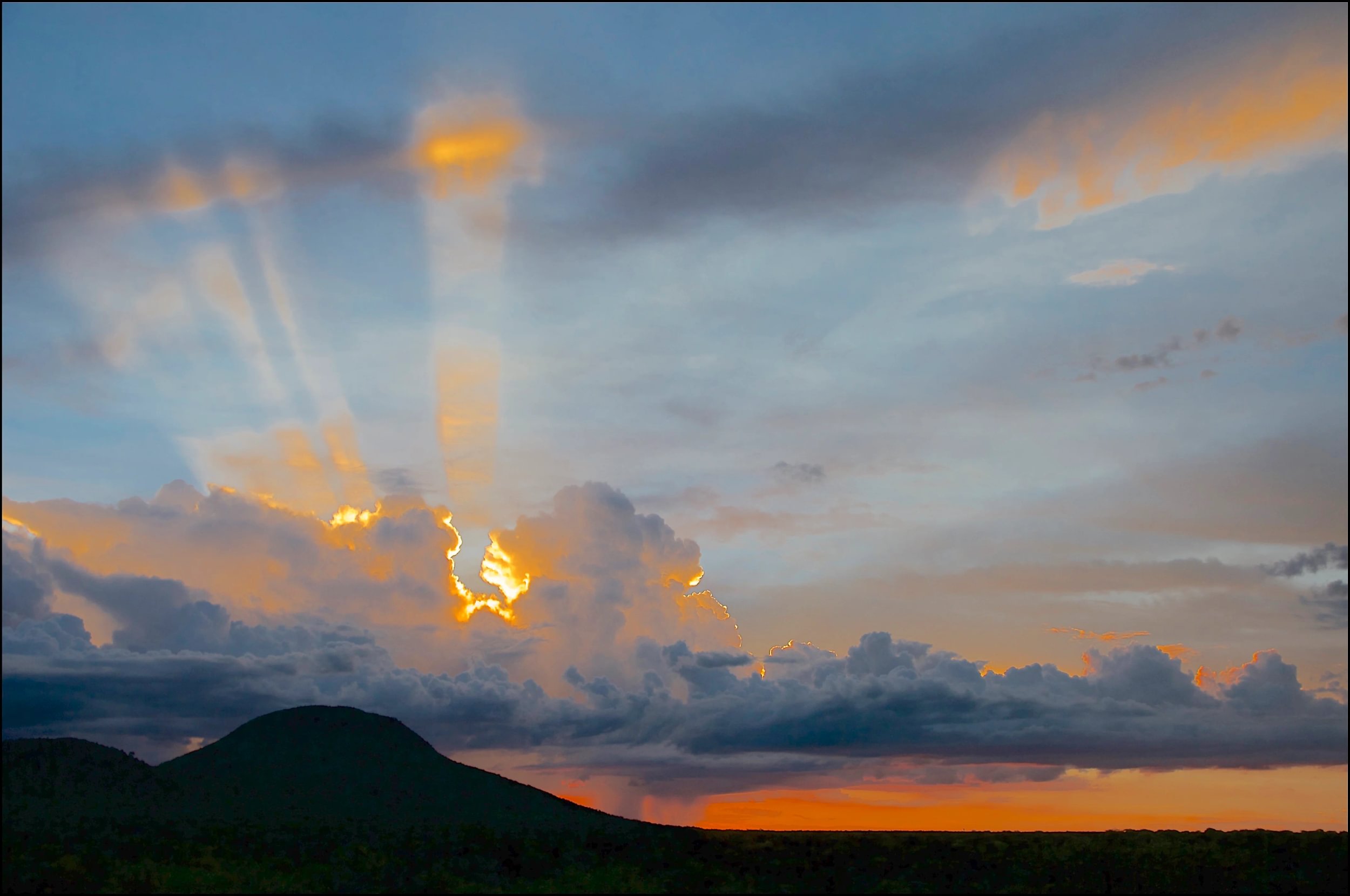 Dunkle Wolken mit der Sonne dahinter über dem Okonjima Nature Reserve in Namibia mit Bergen im Vordergrund