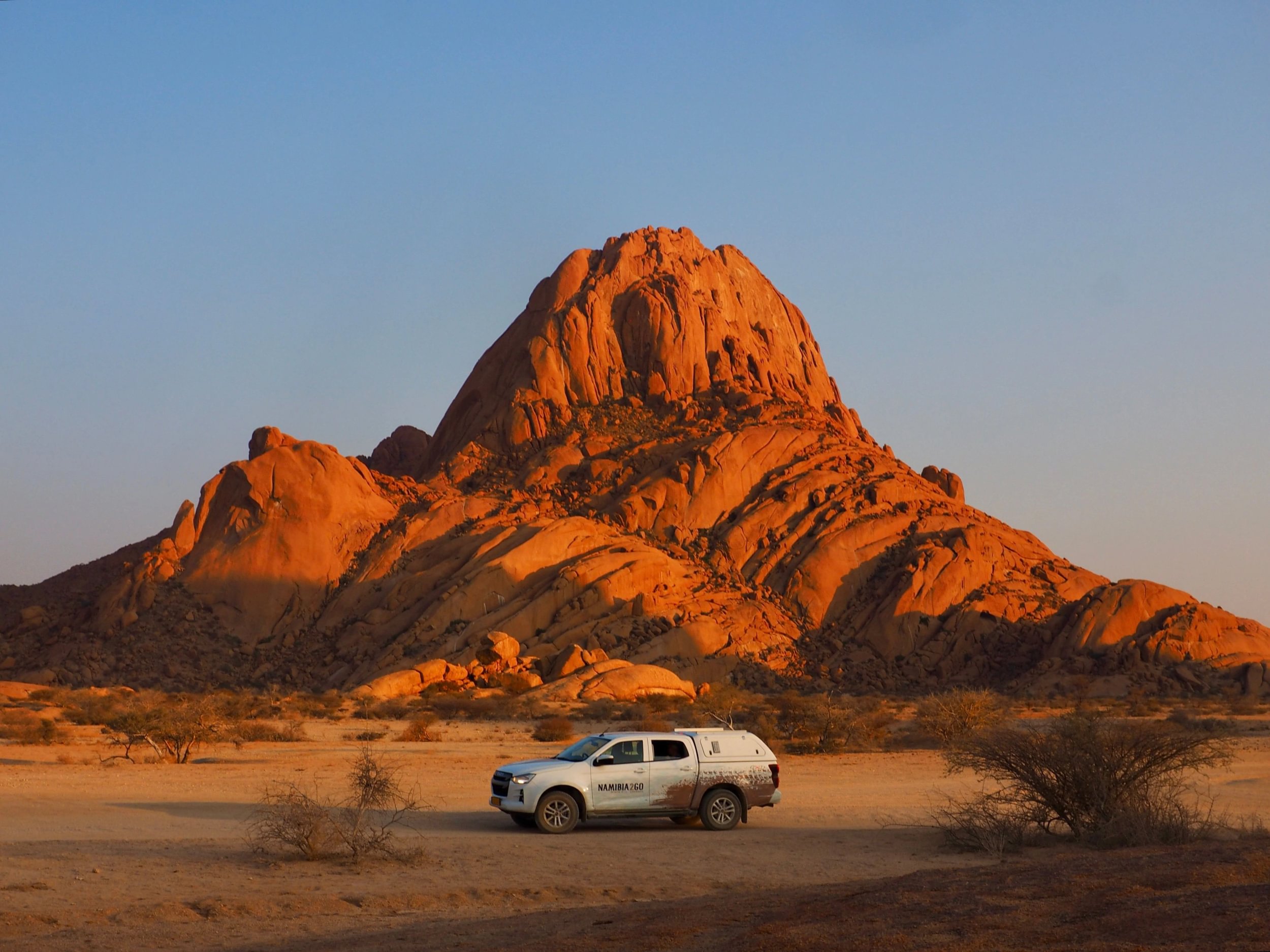 Safari-Jeep steht bei Spitzkoppe vor einem Felsen bei Sonnenuntergang